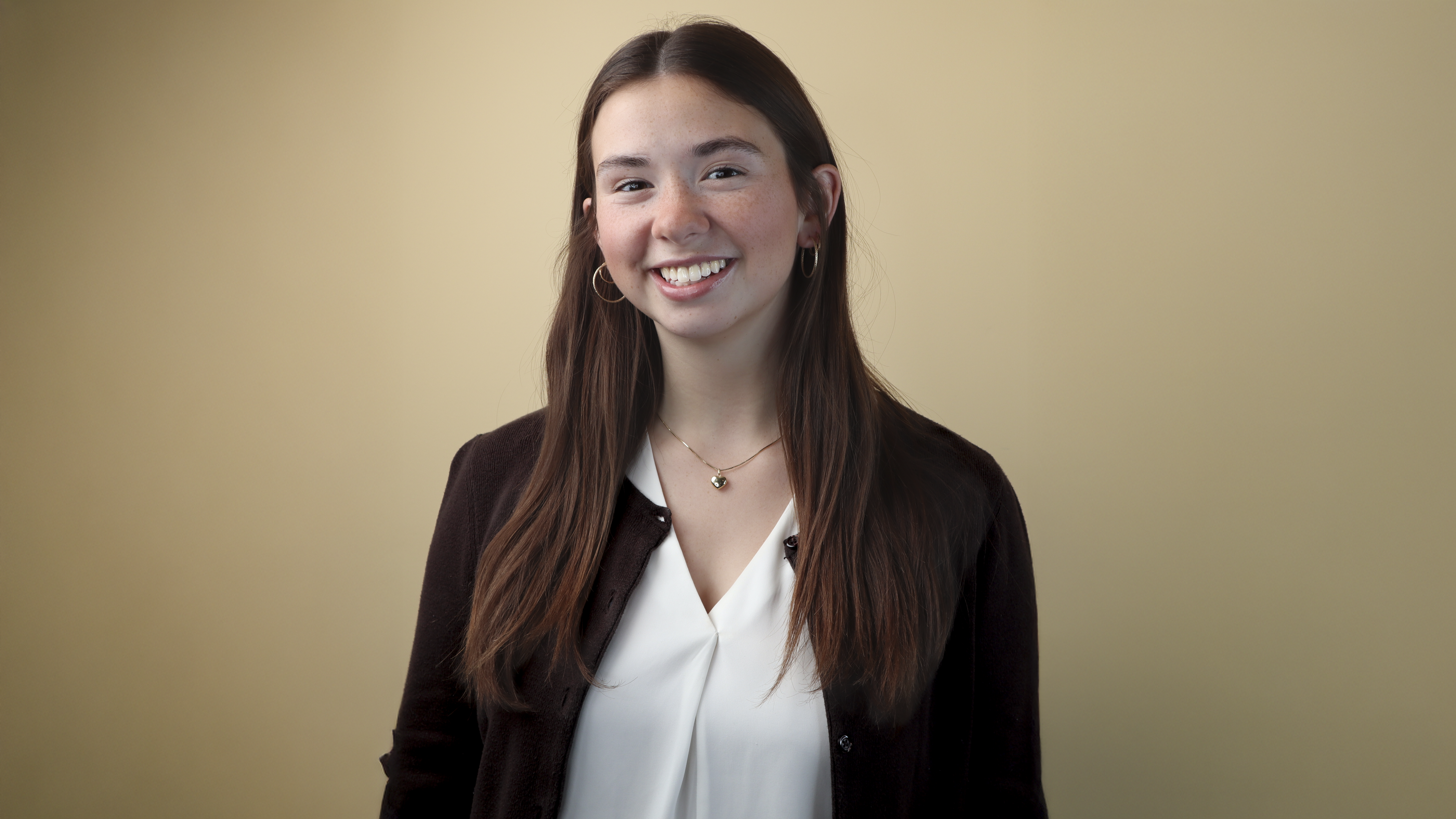 Grace Yoder wears a white button up shirt and black blazer while smiling in front of a beige background. Grace Yoder wears a white button up shirt and black blazer while smiling in front of a beige background.